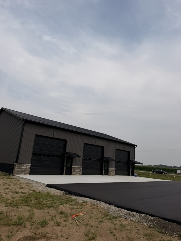 Building 1 garage-door side — gray siding, black trim, stone wainscoting, and paved approach