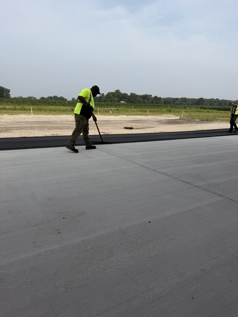 A1-Asphalt worker smoothing fresh asphalt with a lute — a long-handled flat-blade tool, not a broom