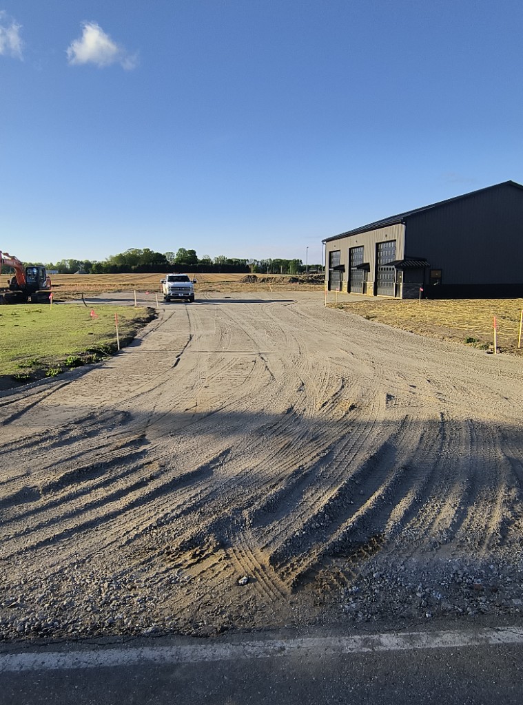 Today — gravel and dirt lot with tire tracks in front of Building 1