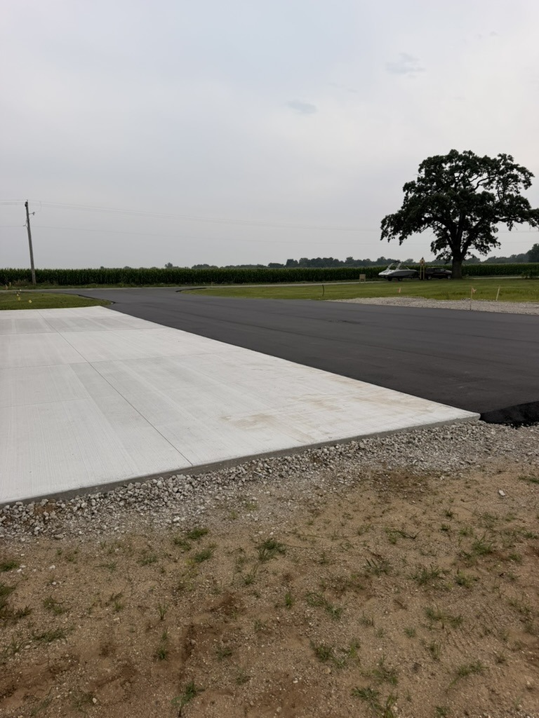 Clean seam where fresh black asphalt meets the concrete apron and gravel edge