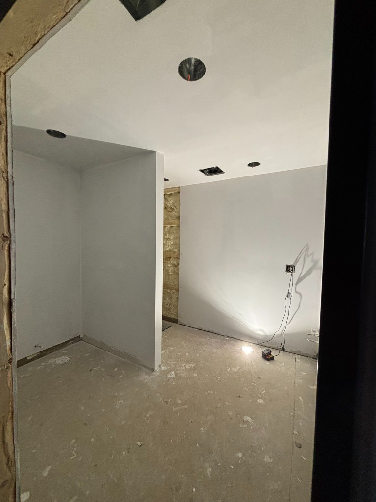 Bathroom interior — freshly drywalled walls, shower niche framed out, recessed lights and exhaust roughed in