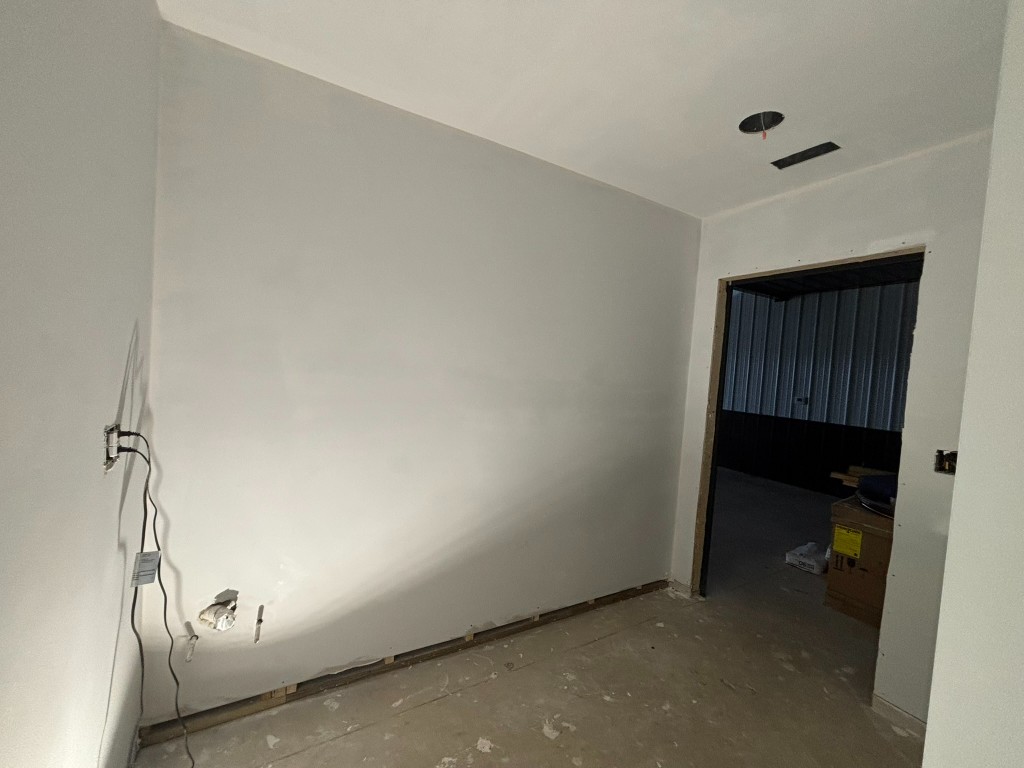 Bathroom after first coat — clean white walls, doorway looking out into the main garage bay
