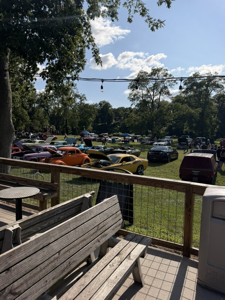 Car show field viewed from Front Street Pizza Pub patio with string lights and hog-wire railing