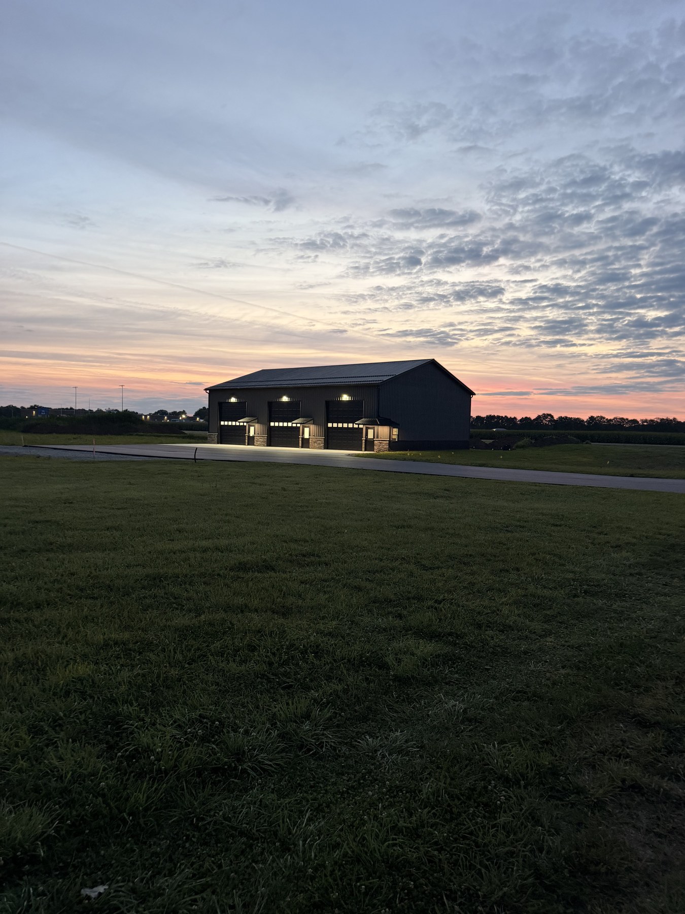 Building 1 at sunrise — three upgraded garage bays lit, fresh asphalt, orange-pink horizon on Kamp Kozy