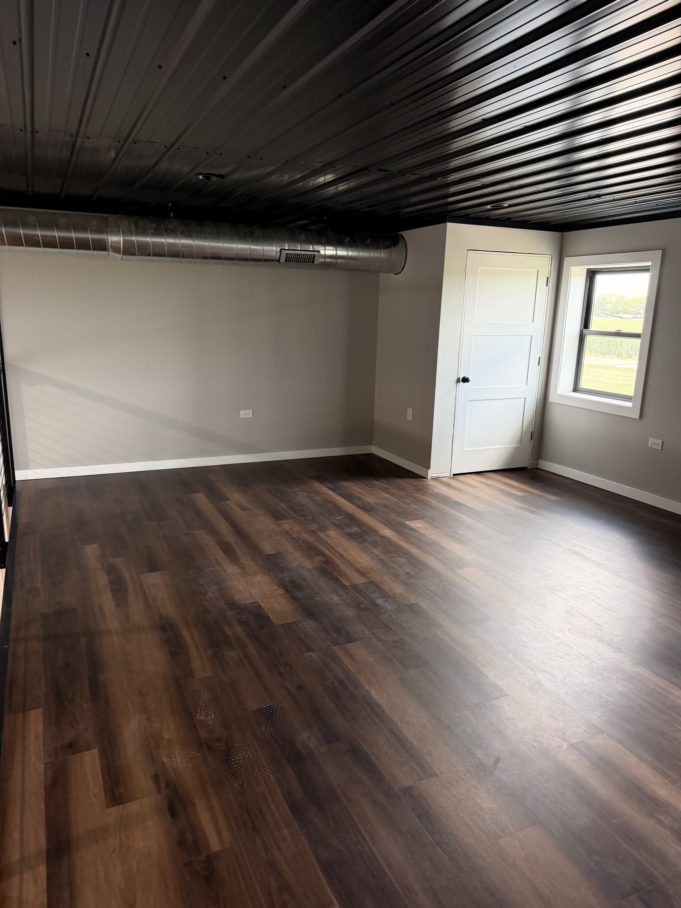 Finished interior room with wood-look floor, gray walls, black corrugated ceiling, and white interior door