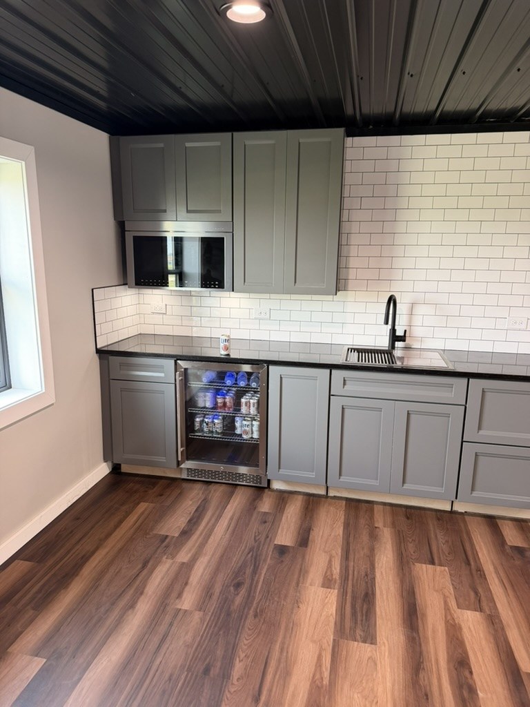 Kitchenette beverage fridge installed in mezzanine — Miller Lite stocked, black faucet and sink, industrial metal ceiling