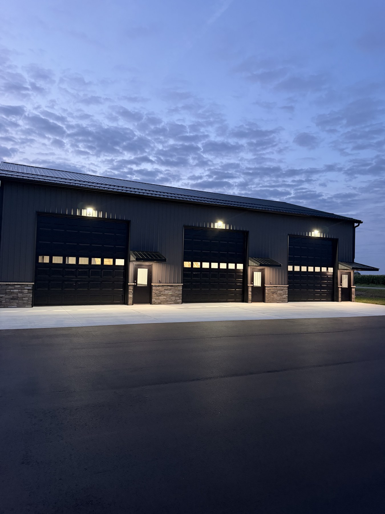 Building 1 at dawn — upgraded garage doors with windows, stone accents, fresh asphalt apron
