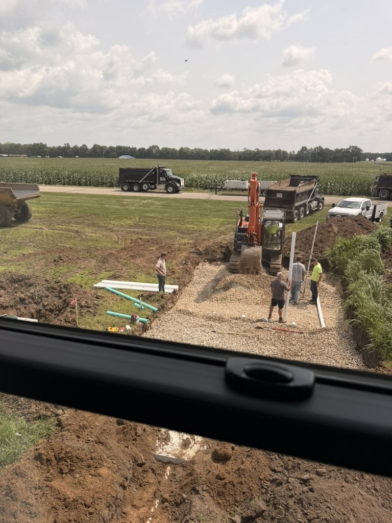 Crew installing septic gravel bed and PVC pipe beside Building 1 — view from unit window