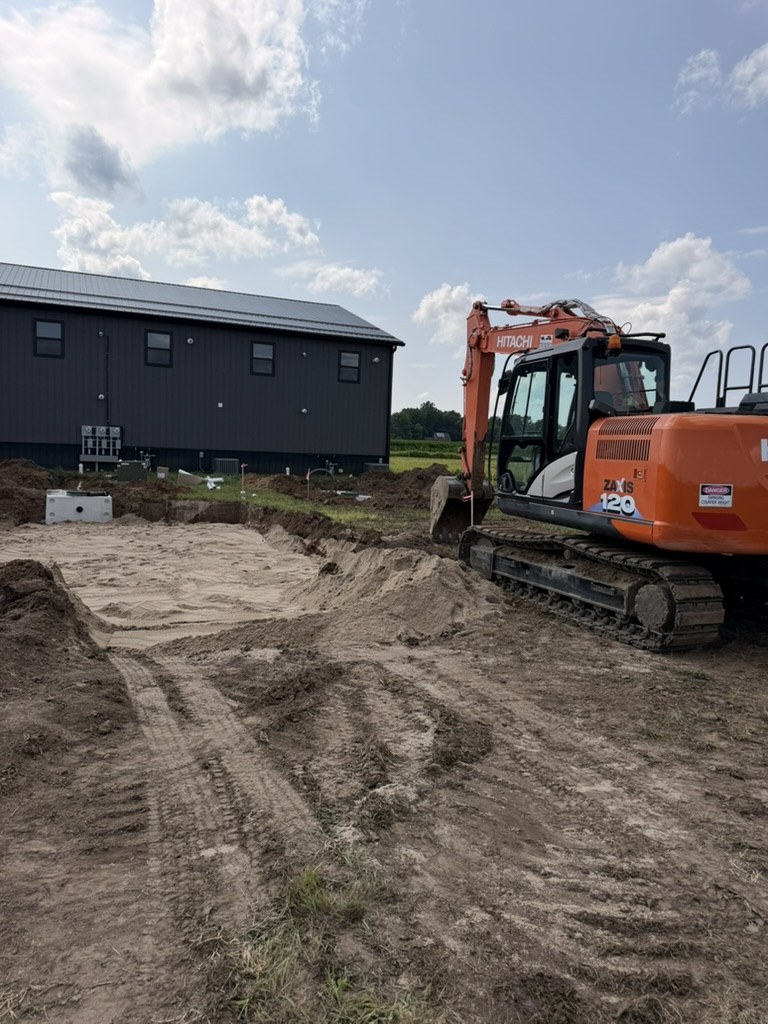 Hitachi excavator beside sand bed and septic tank install next to Building 1