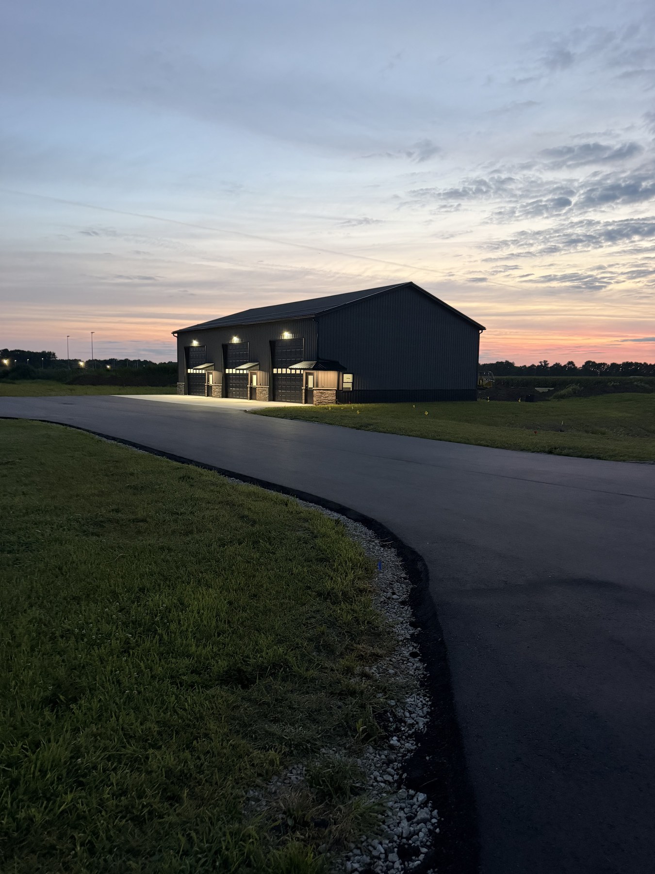 Building 1 at sunrise — three garage bays lit, asphalt lot, orange-pink horizon on Kamp Kozy