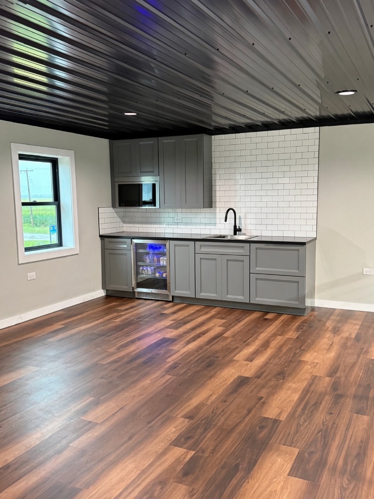 The Lake Bay mezzanine kitchenette — gray cabinets, black counter, subway tile, beverage fridge upstairs