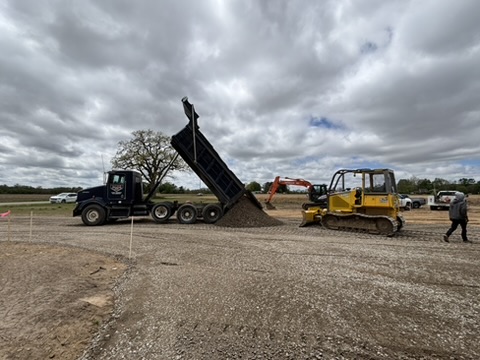 Dump truck raising its bed to drop aggregate onto the parking lot base