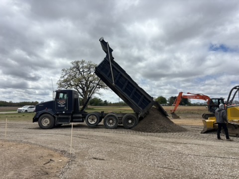 Wide view — dump truck and Hitachi excavator on site with aggregate pile