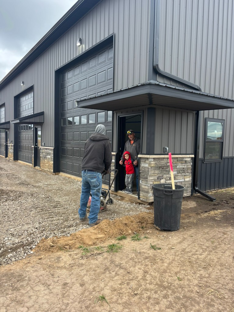 Plate compactor working near Building 1 entrance — detail compaction along the building