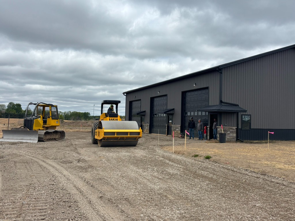 Building 1 site work — Sakai roller and bulldozer compacting the parking lot base in front of three garage bays