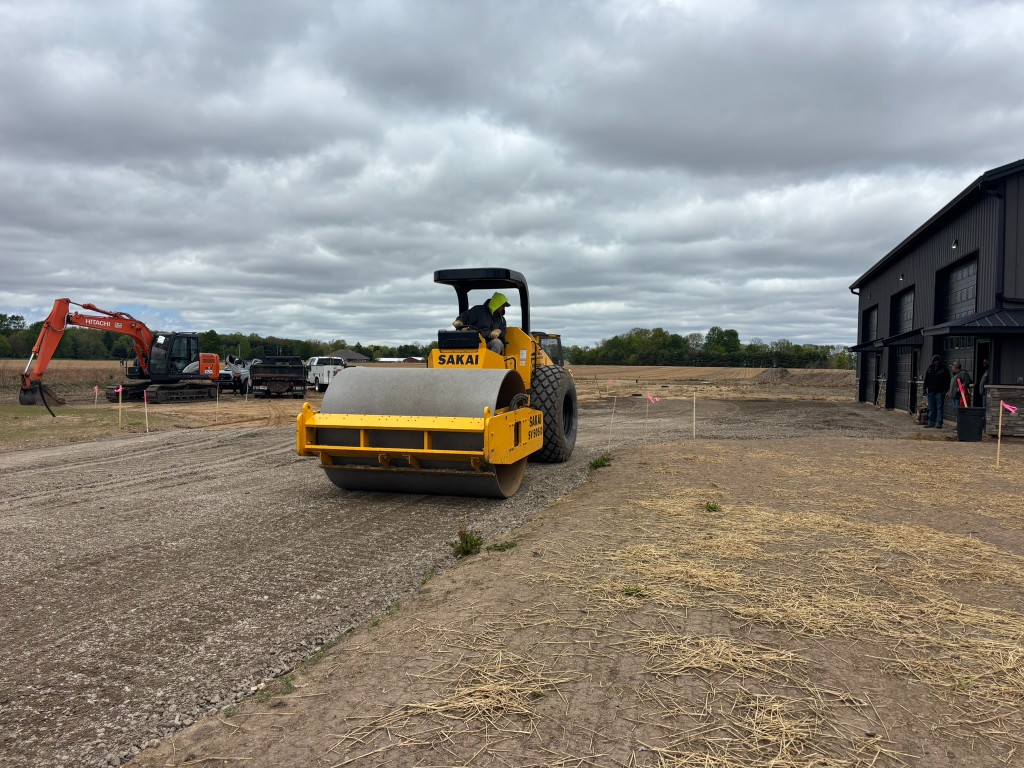 Operator running the Sakai vibratory roller across the compacted gravel base