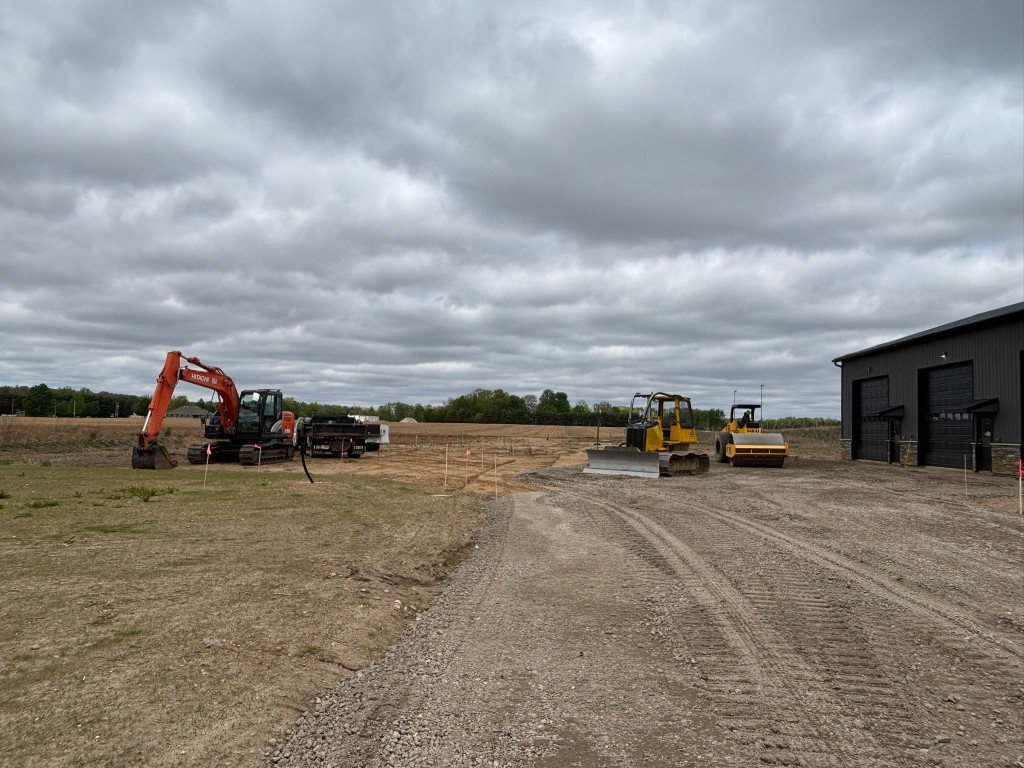 Wide site overview — Hitachi excavator, bulldozer, Sakai roller, and Building 1 with three garage bays
