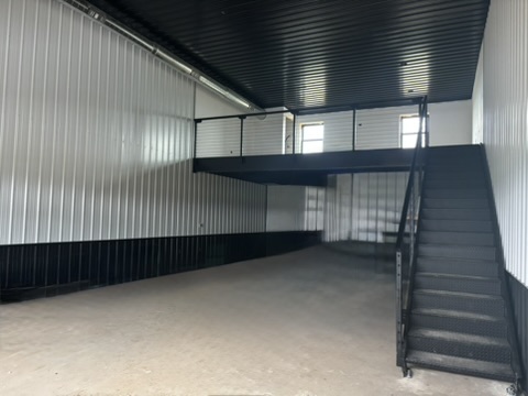 Main floor wide shot — black steel stairs, mezzanine platform, white corrugated walls with black wainscoting