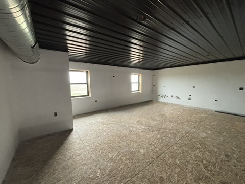 Mezzanine interior — OSB subfloor, drywalled walls, black metal ceiling with HVAC ductwork, natural light from windows