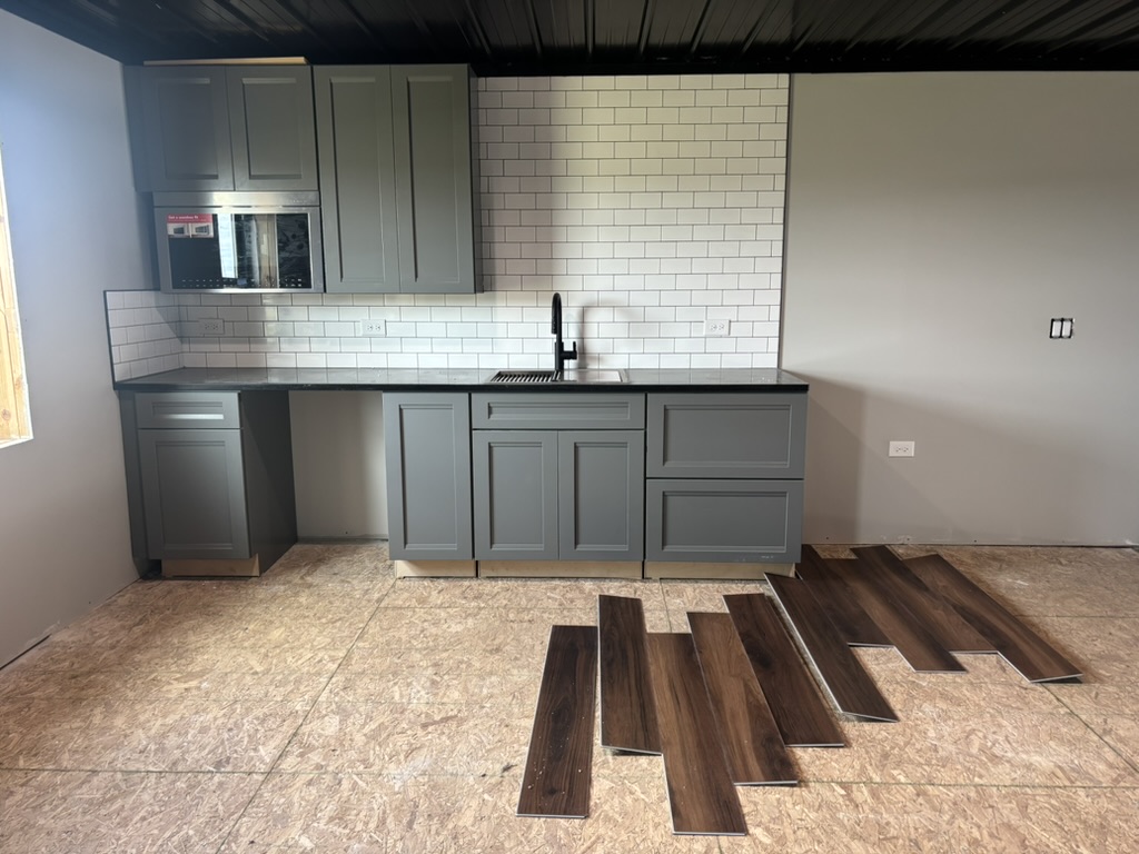 Kitchenette under construction — charcoal shaker cabinets, black countertop, white subway tile backsplash