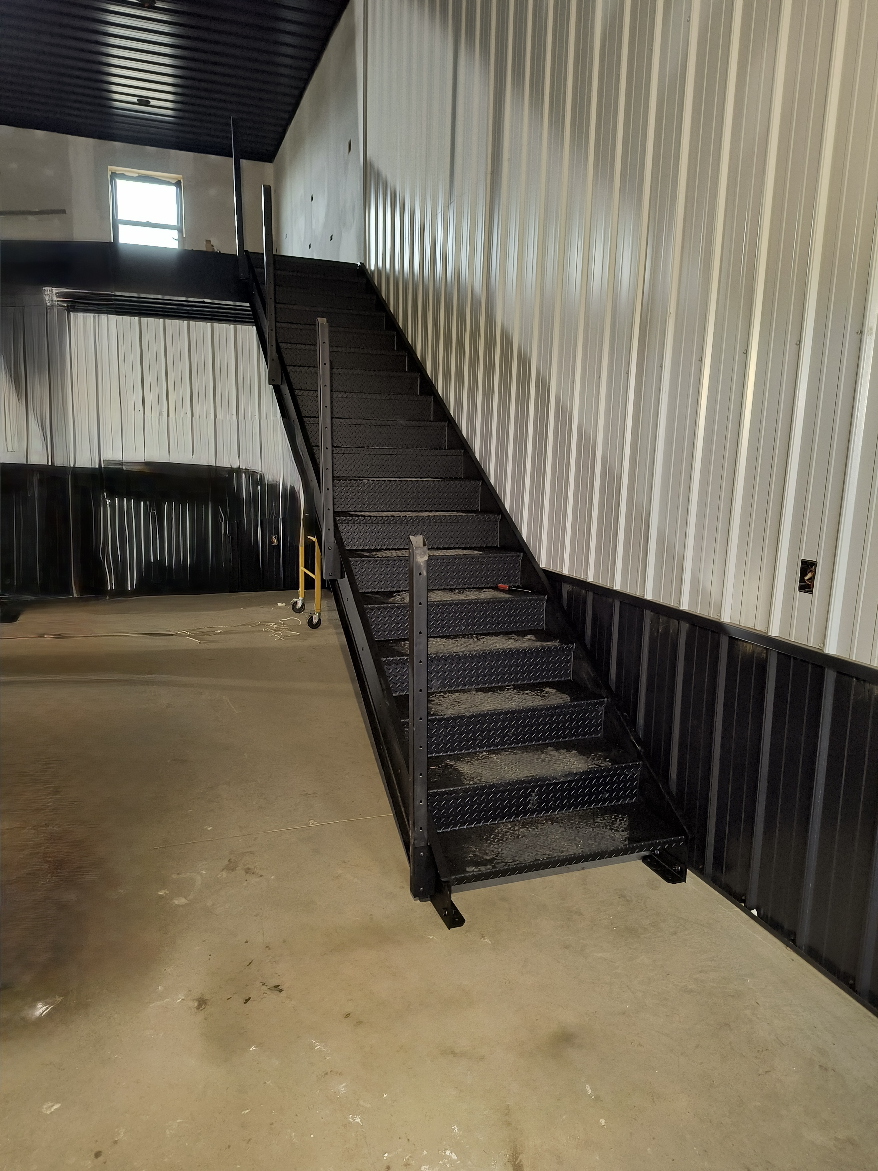 Black steel staircase from the main floor — diamond plate treads running up to the mezzanine
