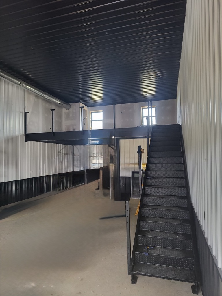 Full Unit 1 interior — mezzanine, black steel stairs, black ceiling, windows, and 1,200 sq ft main floor