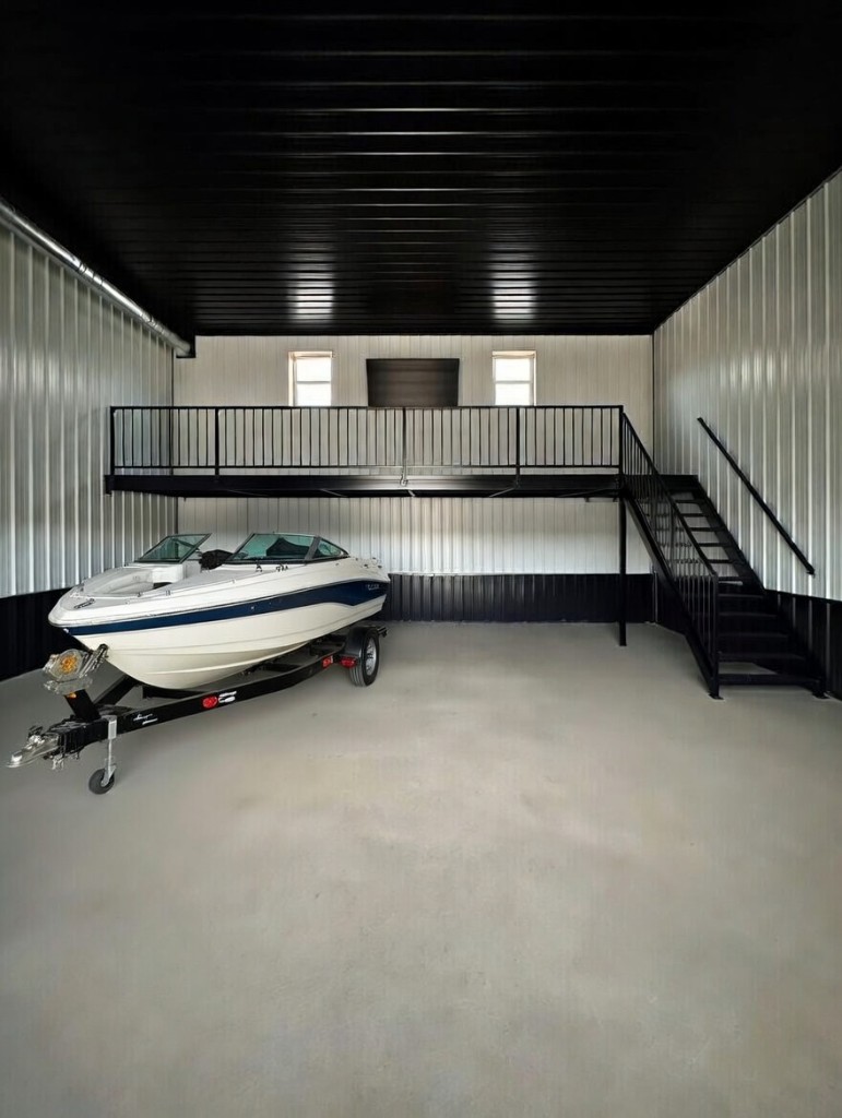 Interior of a Diamond Garage Condo unit with a boat on a trailer, metal mezzanine, and two-tone corrugated walls
